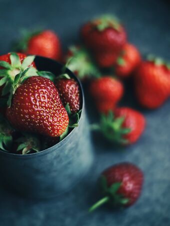 Ripe strawberries scattered around an iron mug. Dark photoの写真素材