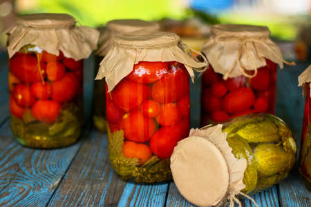 Pickled tomatoes in a glass jar on an old wooden table. Summer harvest canning.