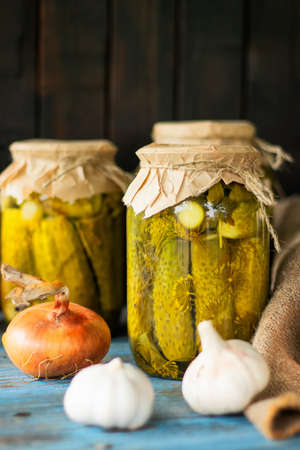 Pickled tomatoes and cucumbers in glass jars on an old wooden table.の写真素材