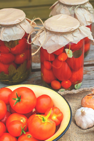 Pickled tomatoes and cucumbers in glass jars on an old wooden table.の写真素材