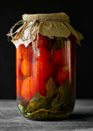 Pickled tomatoes in a glass jar on a dark background. View from above. Summer harvest canning.の写真素材
