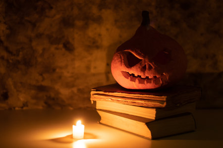 Festive scary halloween pumpkin on a stack of old books with candlesの写真素材