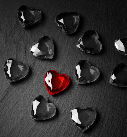 A red crystal in the shape of a heart lies on a dark background among black and white crystals.の写真素材
