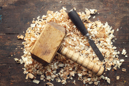 Carpenters wooden mallet and chisel lie on a workbench with wood shavingsの写真素材
