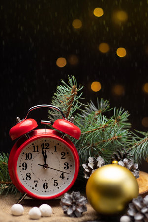 Red retro alarm clock with fir branches and a Christmas tree toy. The clock shows a few minutes until New Year.の写真素材