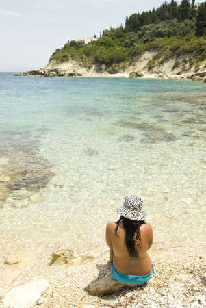Asian woman sitting on a rocky beach.の写真素材