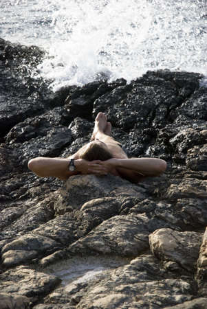 man sunbathing on rocks next to the sea.の写真素材