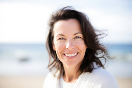 Serene beach portrait of a smiling 50-year-old brunette in light-colored clothing and a white wool sweaterの写真素材