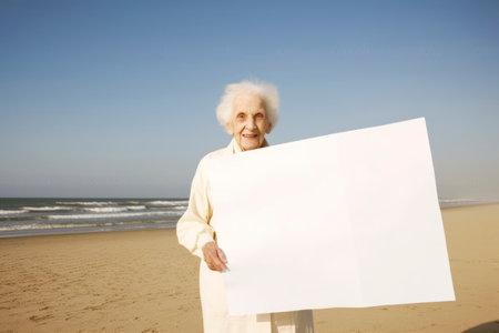 Senior woman holding a blank sheet of paper on the beach at the day timeの素材