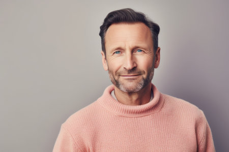 Portrait of a handsome mature man in a pink sweater on a gray backgroundの素材