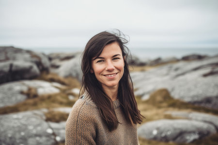 Portrait of a smiling young woman with long brown hair standing on a rock in the Scottish Highlandsの素材