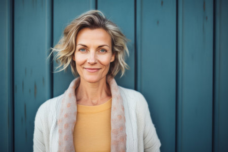 Portrait of smiling mature woman standing against blue wooden wall at homeの素材