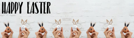 Easter background banner panorama greeting card - Young women holding Easter eggs with bunny ears / Easter bunnies in their hands, isolated on white vintage shabby wall textureの写真素材