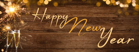 HAPPY NEW YEAR 2022 - Festive silvester background panorama banner long - Golden yellow fireworks, sparklers  and champagne classes toasting on rustic brown wooden wall texture with bokeh lightsの写真素材