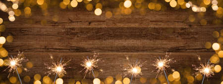 Golden bokeh light and burning sparkler, isolated on rustic brown wooden texture - Holiday New Year's Eve Silvester New Year Party Christmas festive background banner greeting cardの写真素材
