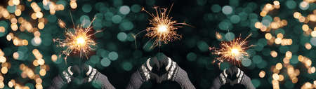 Silvester / Party / New Year background banner panorama - Happy people hold sparkling sparklers in their hands, hands heart shape, gloves with scandinavian pattern in the dark night with turquoise bokehの写真素材