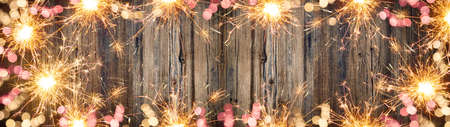 Frame made bokeh lights, sparklers and fireworks isolated on rustic wooden table texture - holiday New Year's Eve background banner, top view with space for textの写真素材