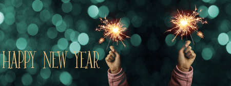 Happy New Year 2022 background banner panorama - Happy girl hold sparkling sparklers in her hands at dark night with turquoise bokeh lights, New Year's Eveの写真素材