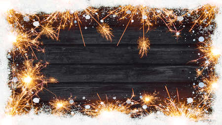 Silvester, New Year Christmas or other festive holiday celebration background - Frame made of snow, snowflakes, sparklers and bokeh lights, on rustic black wooden table wall boards wood texture, top viewの写真素材