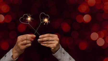 Valentine's Day / Love / Wedding / Birthday / Silvester / New Year / Party background - happy woman holding an sparkling heart sparklers in her hands, at night with red bokeh lightsの写真素材