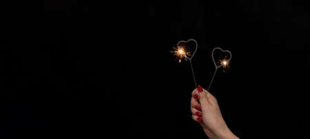 Valentine's Day / Love / Wedding / Birthday / Silvester / New Year / Party background banner - Happy woman holding sparkling heart sparklers in her hand, with red colored nails at black nightの写真素材