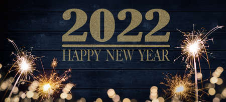 HAPPY NEW YEAR 2022: Golden bokeh lights flares and sparkler isolated on rustic blue colored wooden...