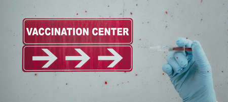 CORONAVIRUS CORONA COVID-19 VACCINATION: Red sign and arrows with the inscription VACCINATION CENTER and doctor with syringe with corona vaccine in his handの写真素材