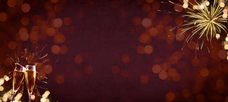 HAPPY NEW YEAR 2022 / New Year's Eve Holiday Event Party Firework - Festive silvester background panorama banner - Golden fireworks and champagne classes toasting on dark red night sky texture with bokehの写真素材
