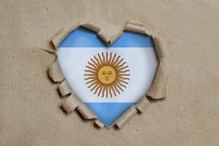 Heart shaped hole torn through paper, showing Argentina flagの写真素材