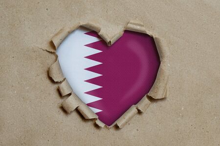 Heart shaped hole torn through paper, showing Qatar flagの写真素材