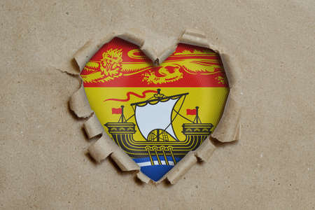 Heart shaped hole torn through paper, showing New Brunswick flagの写真素材