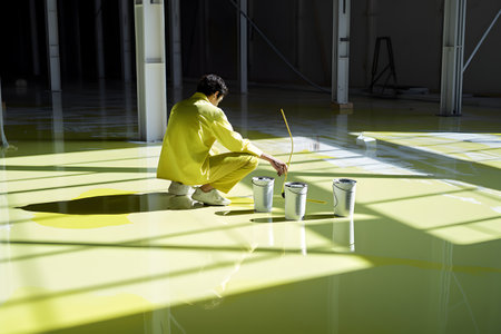 Man in yellow suit sitting on floor with paint bucket and paint rollerの素材