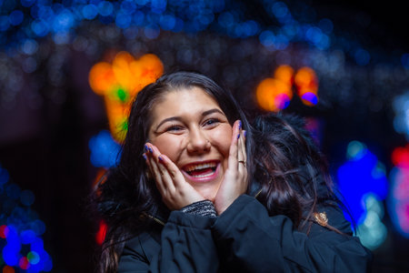 Happy girl reacts to uncovering a Christmas surprise with bokeh Christmas lights in background.