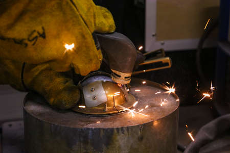 A worker cutting through metal with using a welding gun and safety gloves.
