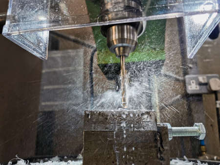Industrial image of a pillar drill machine which has its drill bit surrounded by smoke and drops...