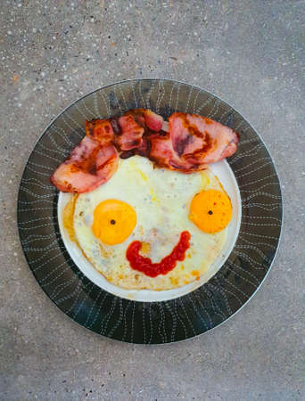 Fried eggs with bacon and ketchup designed as a smiley face to start the day with a positive mood.