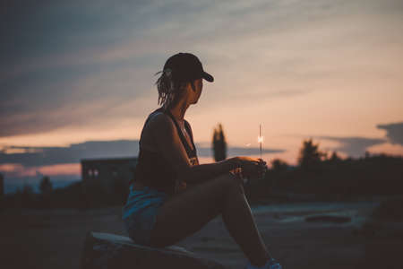 Portrait of young european girl holding sparkle stick under the patio outdoor. Happy smiling woman celebrating with fireworksの写真素材