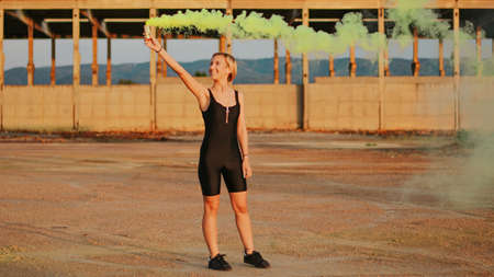 happy young woman having fun with colorful powder cloud. girl running with yellow color smoke bombの写真素材