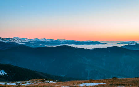 Mountain range with visible silhouettes through the morning colorful fog.Tarcu Mountains in Romania.の写真素材
