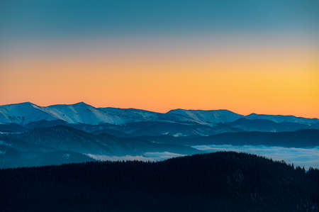 Mountain range with visible silhouettes through the morning colorful fog.Tarcu Mountains in Romania.の写真素材