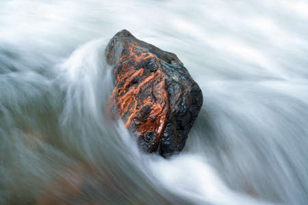 Stone in a stream with water blurred by long exposureの写真素材