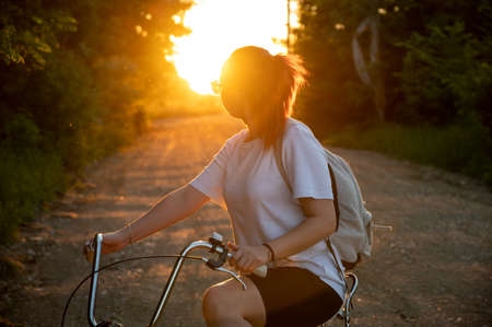 Sport girl with a bike enjoys the view of sunset over an spring forest.の写真素材