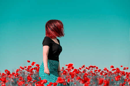 young girl with red hair dressed in a green skirt and a black T-shirt in a poppy field