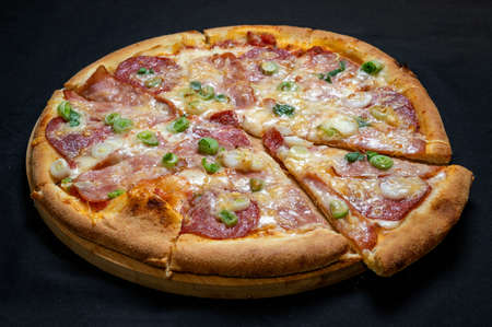 Pizza with green onions, salami, ham, mozzarella and tomato sauce on a black background.の写真素材