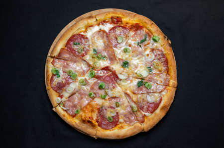 Pizza with green onions, salami, ham, mozzarella and tomato sauce on a black background.の写真素材