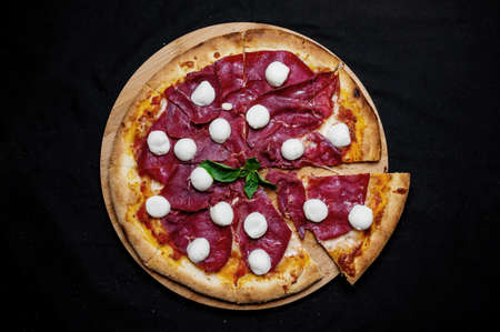 Pizza with tomato sauce, mozzarella and smoked ham on a black background.の写真素材