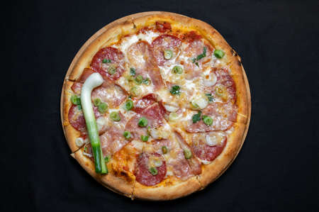 Pizza with green onions, salami, ham, mozzarella and tomato sauce on a black background.の写真素材