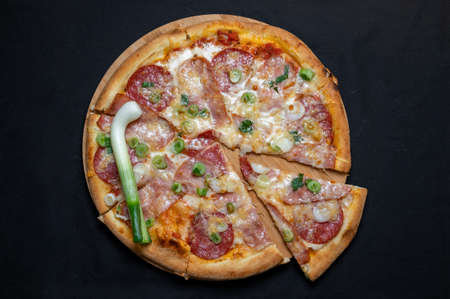 Pizza with green onions, salami, ham, mozzarella and tomato sauce on a black background.の写真素材