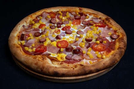 Pizza with tomato sauce, mozzarella, sour cream, salami, pork ham, sausages, corn and cherry tomatoes on a black backgroundの写真素材