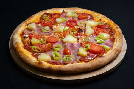 Pizza with tomato sauce, chicken ham, spicy salami, cherry tomatoes, pineapple and hot peppers on a black backgroundの写真素材